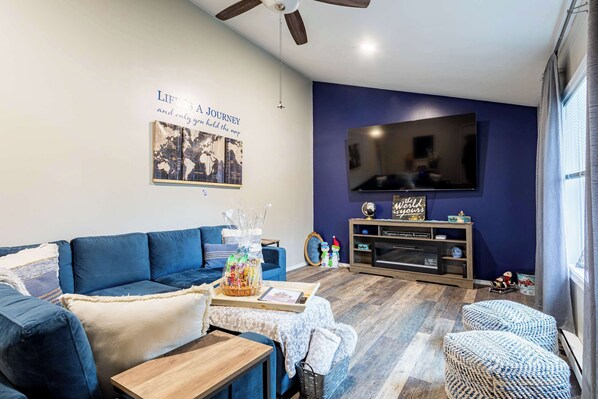 Una sala de estar con un sofá azul, una mesa de centro de madera y una televisión en la pared.