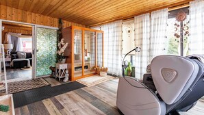 Et hyggeligt rum med træloft, massagestol, skydedør til balkon og grøn beplantning udenfor.
