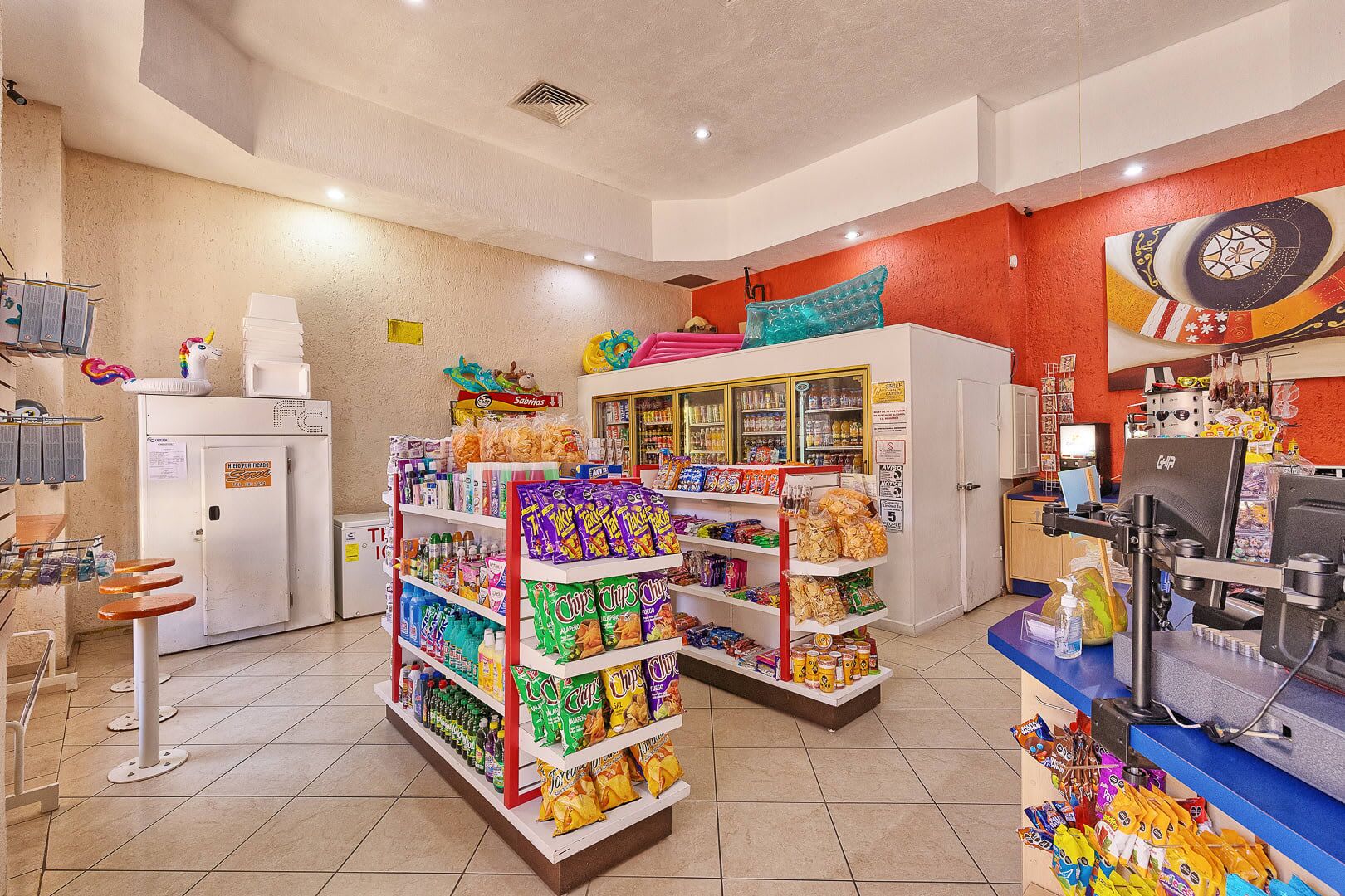 A convenience store with shelves stocked with snacks, a refrigerator, and a cash register.