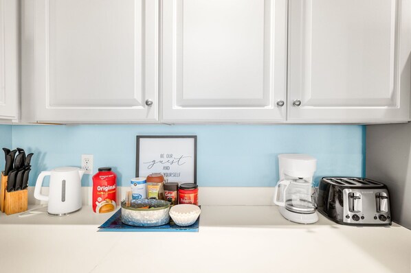 A kitchen counter with a coffee maker, toaster, and various food items. - Pool, Steps to European Village & Trails (Palm Coast)