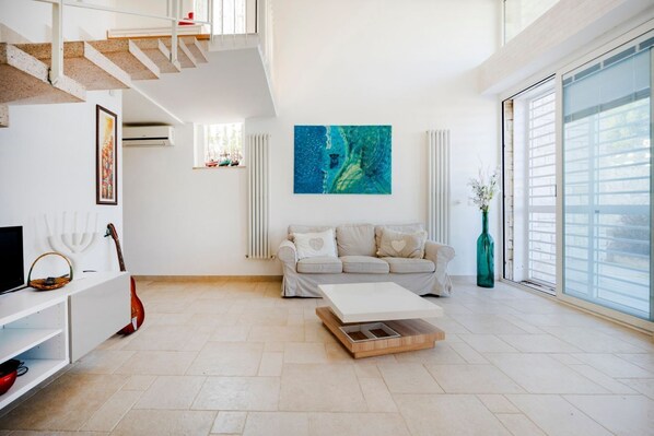 A spacious living room with a staircase, a sofa, a coffee table, and a large window.