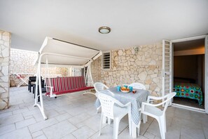 An outdoor patio with a table and chairs, a swing set, and a stone wall.