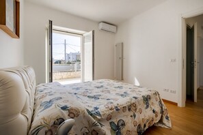 A bedroom with a bed, a window, an air conditioning unit, and a door.