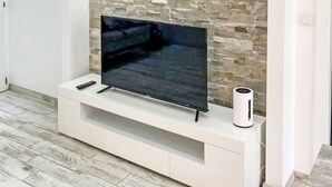 En moderne stue med et fladskærms-tv på et hvidt tv-møbel, en stenvæg og trægulv.