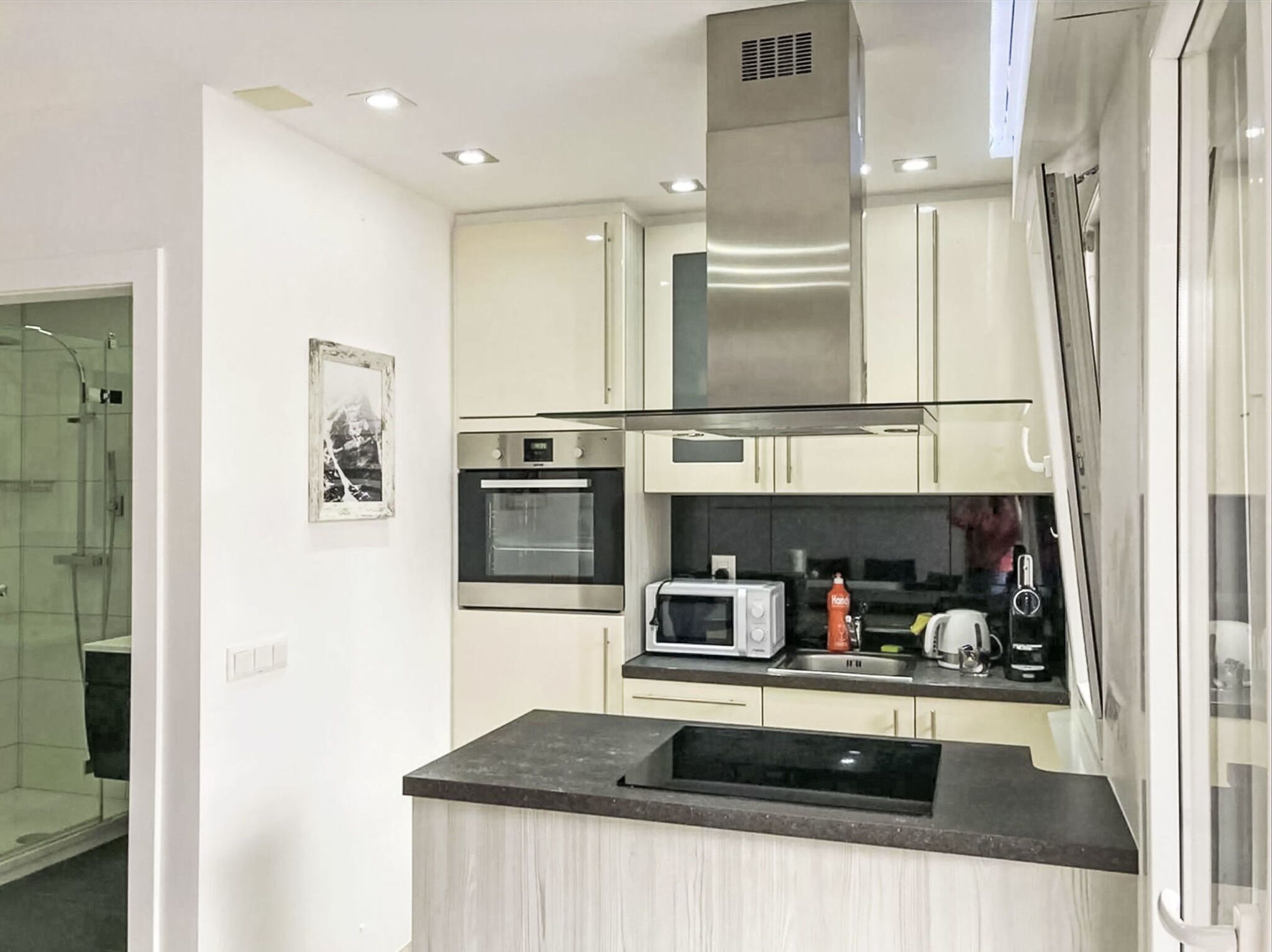 A modern kitchen with white cabinets, a stainless steel range hood, a microwave, and a built-in oven.