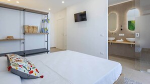 A modern hotel room with a large bed, a TV mounted on the wall, and a bathroom visible through a glass door. - Room Castel Perollo - Camera Verde by Biddizzi Rari - Historic Center in Sciacca (Sciacca)