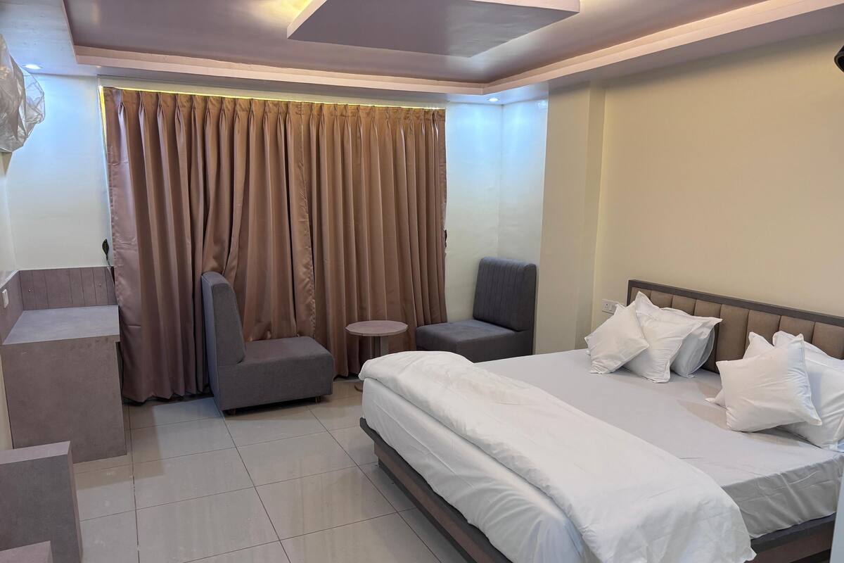 Habitació d'hotel amb un llit gran, una taula rodona petita, un armchair gris i un sofà.