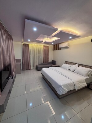 A modern hotel room with a large bed, a sofa, a TV, and a ceiling light fixture. - N.R. Hotel (Shri Madhopur)