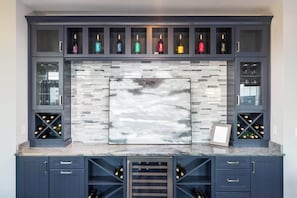 A kitchen with dark blue cabinetry, a tiled backsplash, and wine storage shelves. - Luxury Condo with Sauna, Theater, Elevator, GameRm! (Kill Devil Hills)