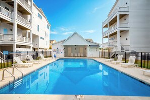 A swimming pool with a 5 ft depth limit, surrounded by white buildings with balconies. - Luxury Condo with Theater, Elevator, GameRm! (Kill Devil Hills)