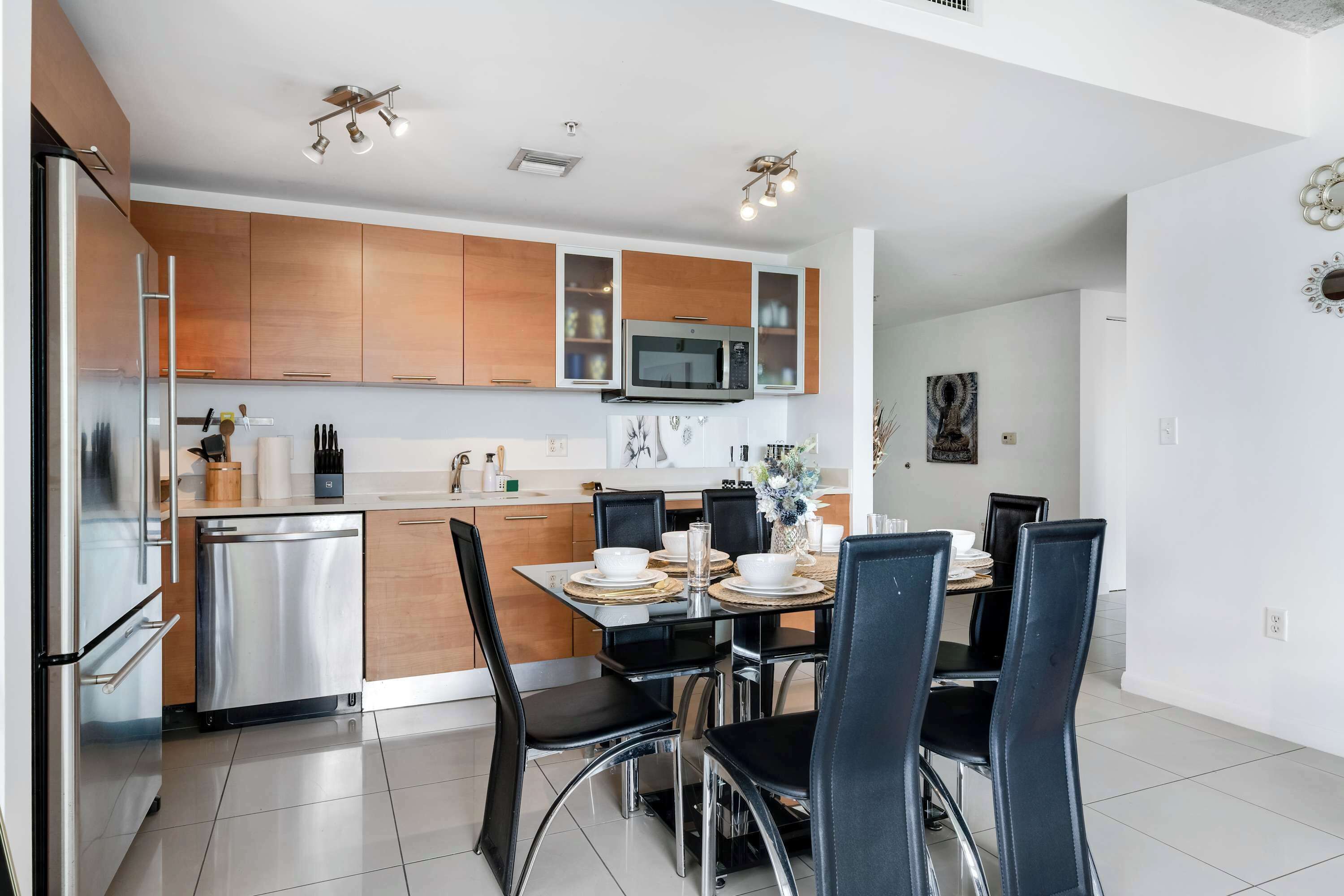 A modern kitchen with stainless steel appliances, wooden cabinets, and a dining area with black chairs and a white table.