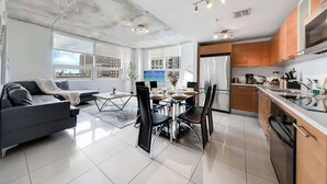 Een moderne woonruimte met een bank, eettafel, stoelen en een keuken met kasten en apparatuur.