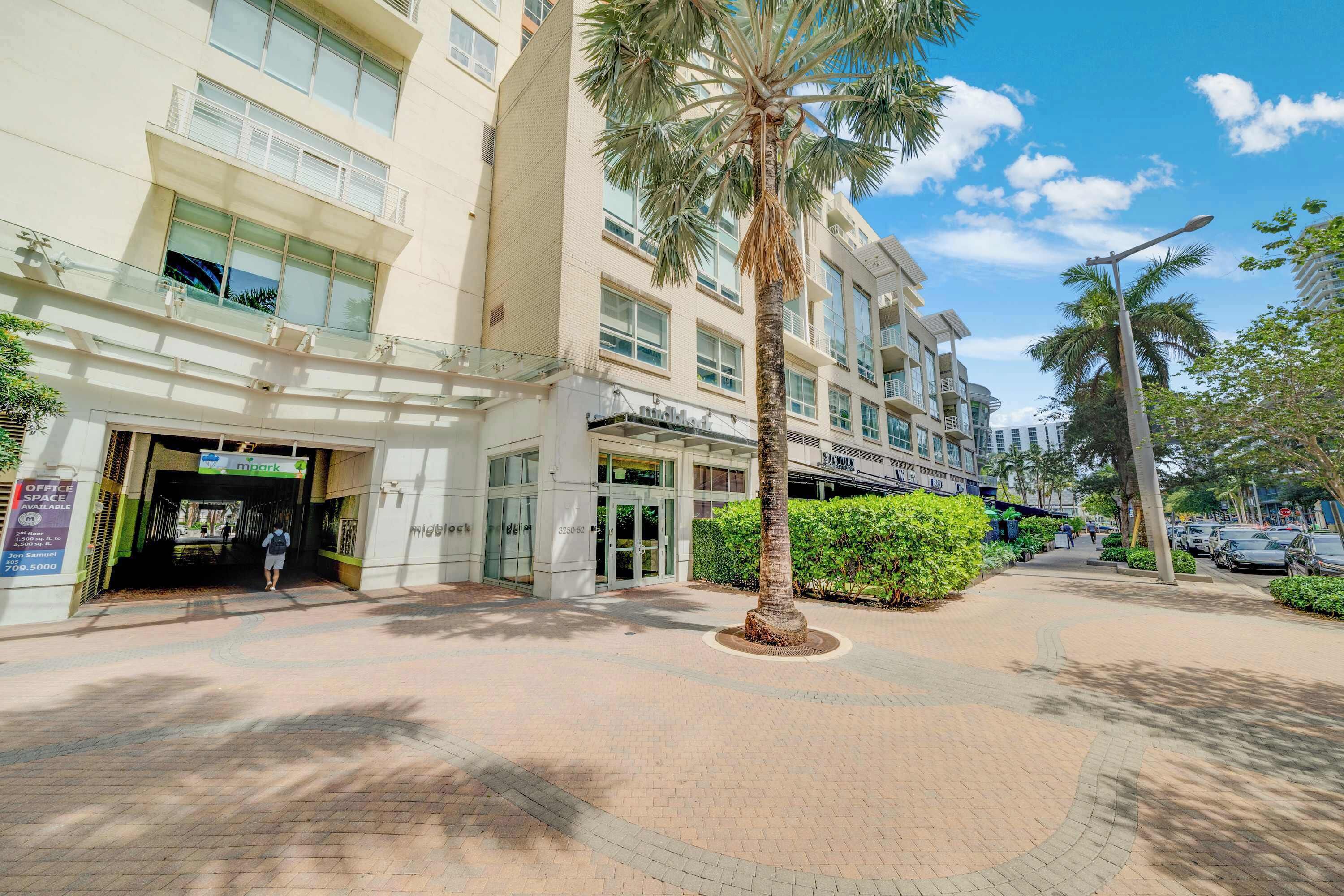 A modern building with a glass entrance, palm trees, and a paved walkway.