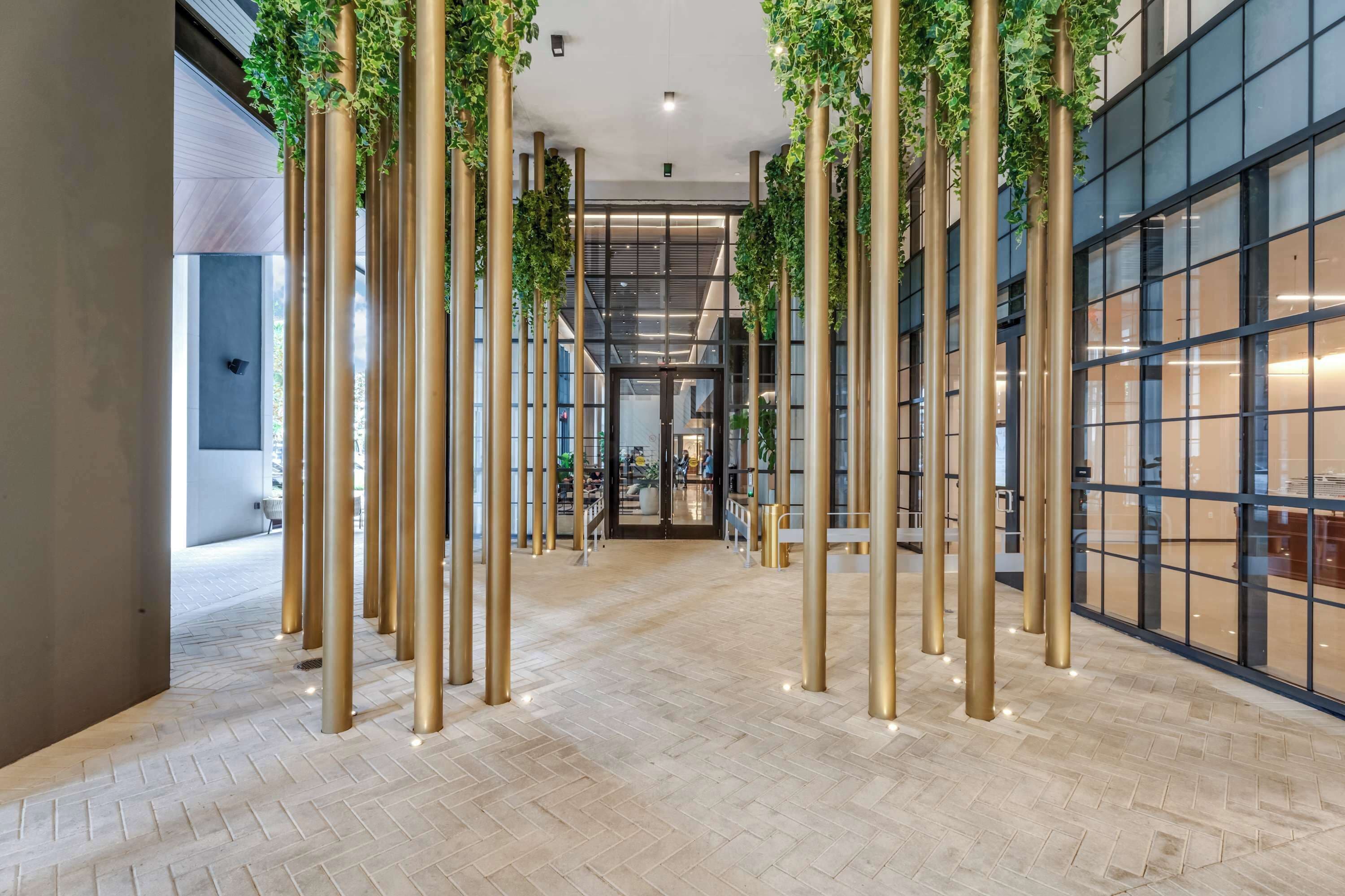 Un interior moderno con suelo de espiga, altas columnas doradas y plantas verdes.