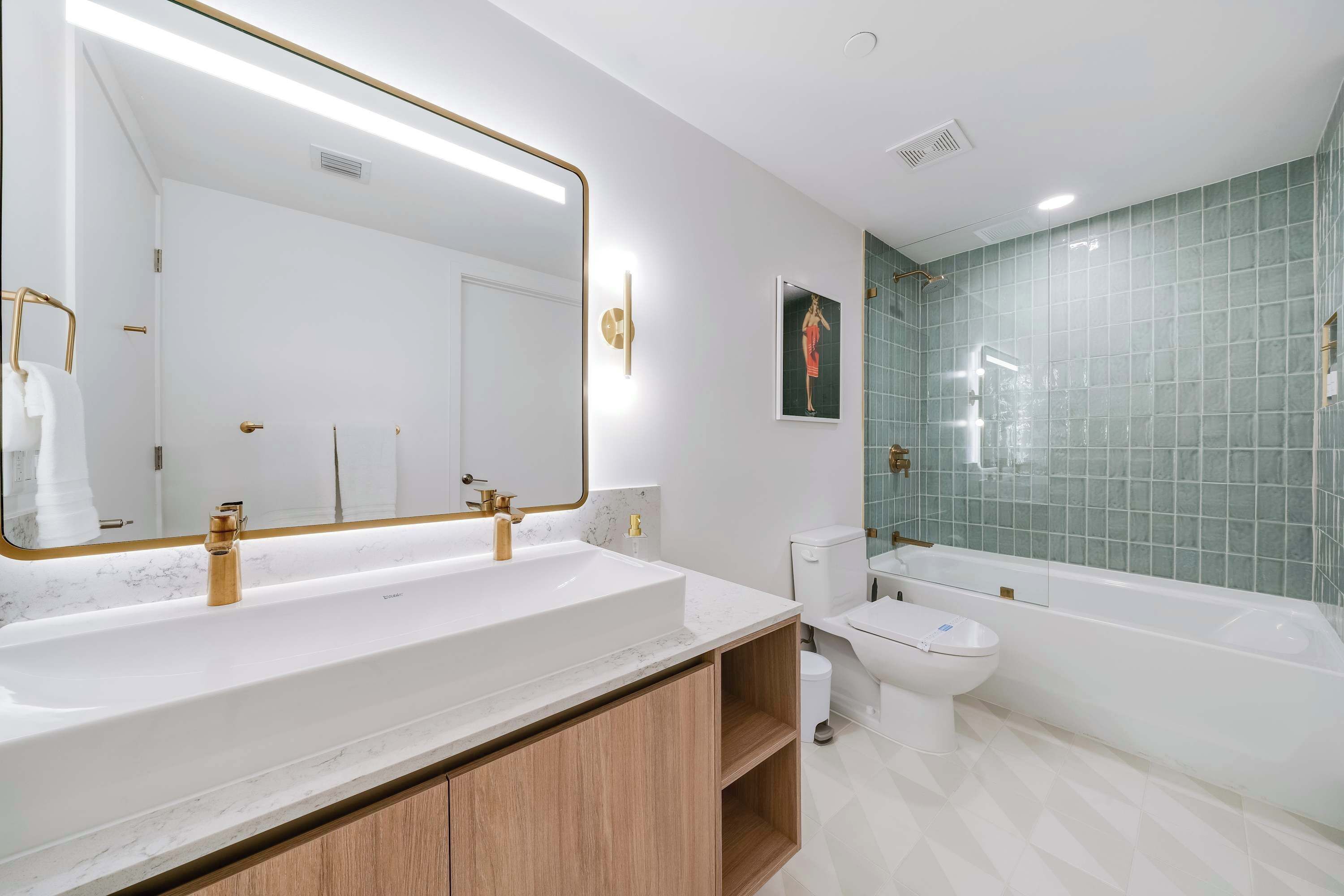Une salle de bain moderne avec un grand miroir, deux vasques, des toilettes et une baignoire.