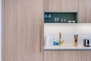 Eine moderne Küche mit Holzschränken, einer integrierten Regalanlage mit Glaswaren, einem goldenen Wasserhahn und einem Toaster.