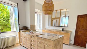 Een ruime keuken met een groot eiland, houten kastjes en een moderne hanglamp.