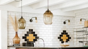Una cucina con isola in legno, sgabelli da bar, zoccolo paraschizzi piastrellato e luci a sospensione.