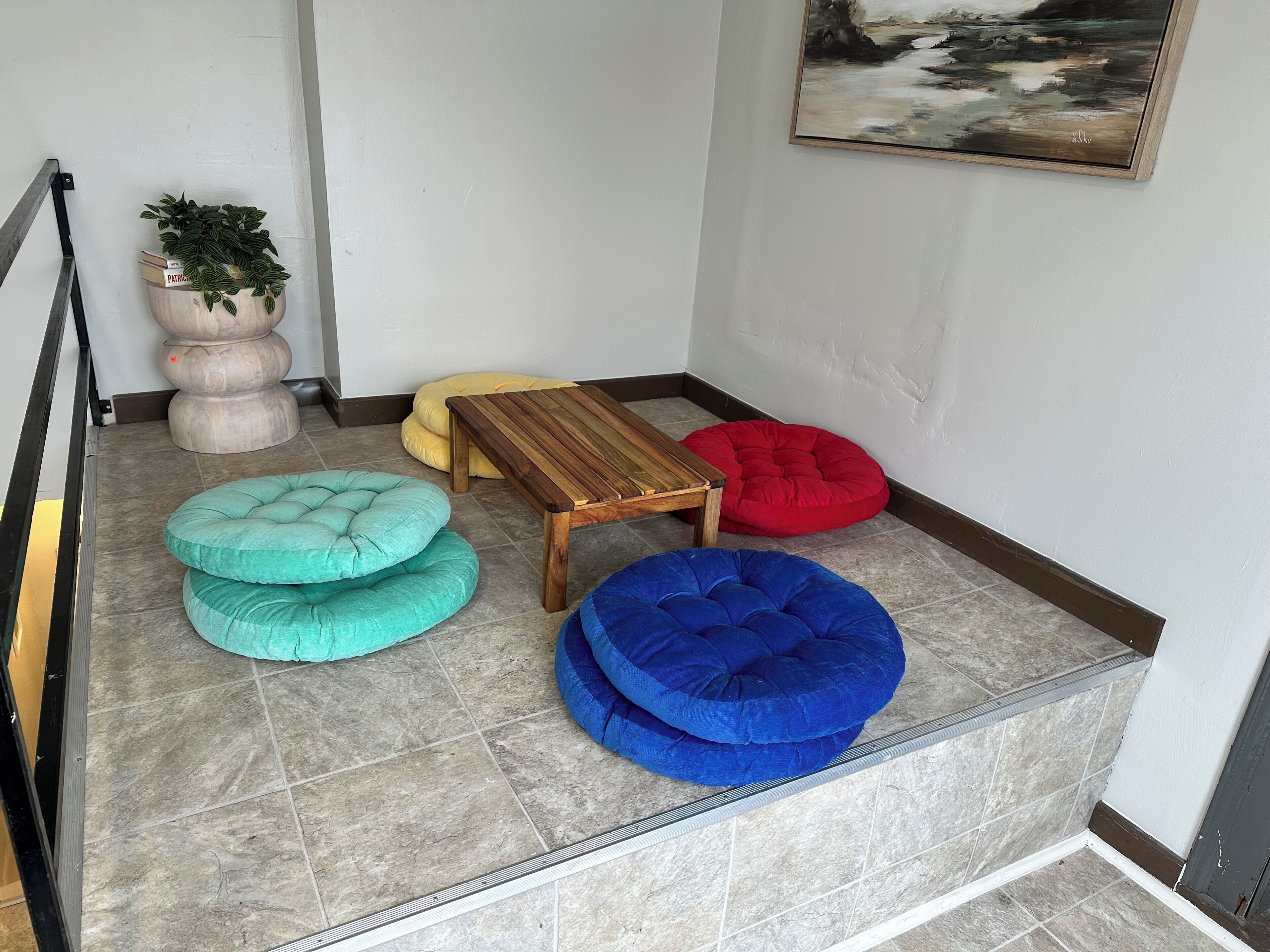 A corner of a room with a wooden table, colorful bean bags, and a potted plant.