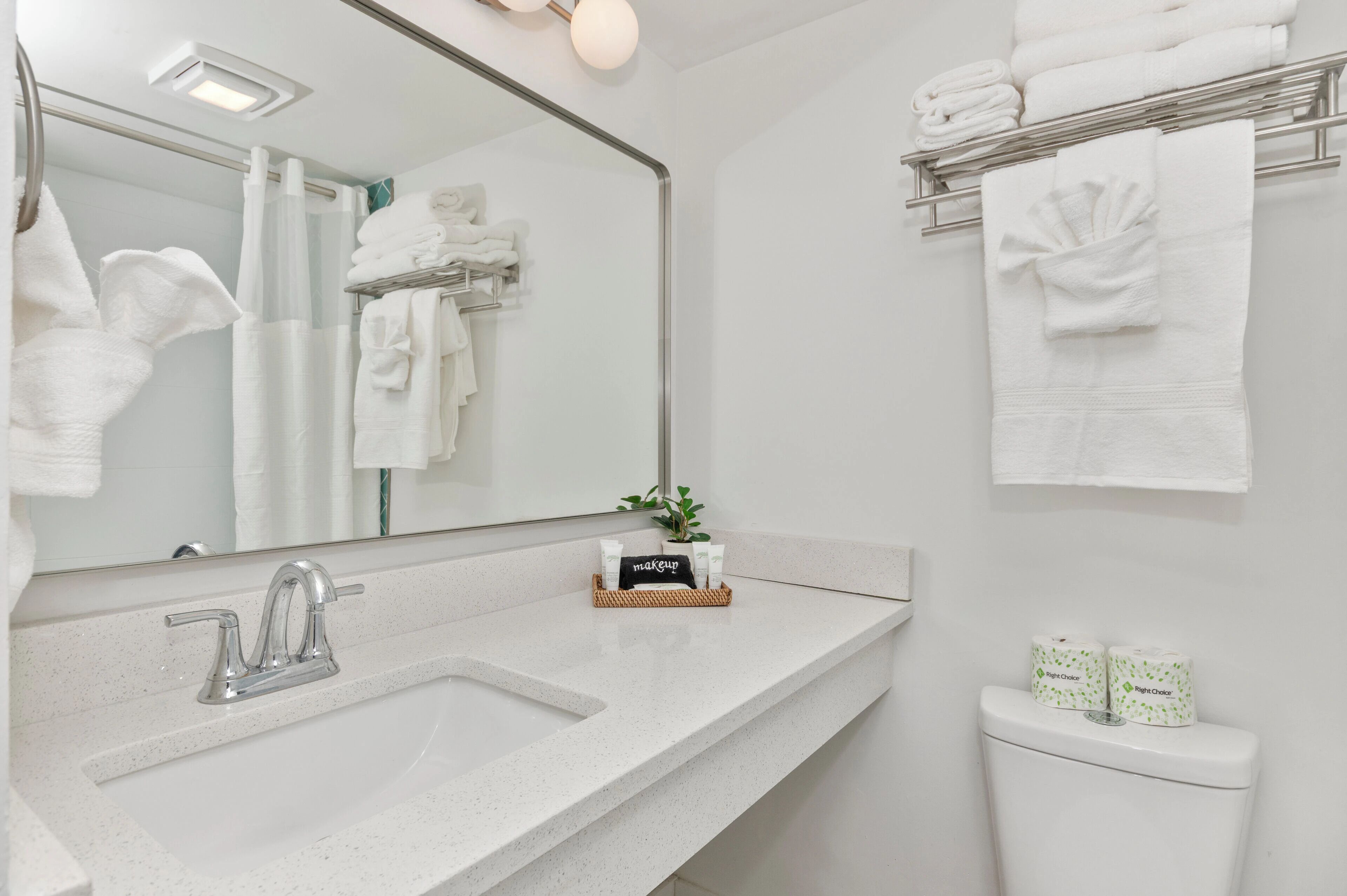A modern bathroom with a large mirror, a sink, and a toilet. There are towels and toiletries on the counter.