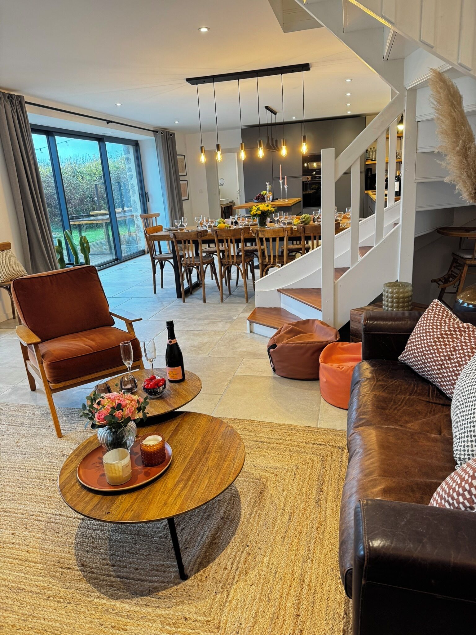 A modern living room with a brown leather sofa, a wooden coffee table with drinks, and a dining area with wooden chairs and a glass table.