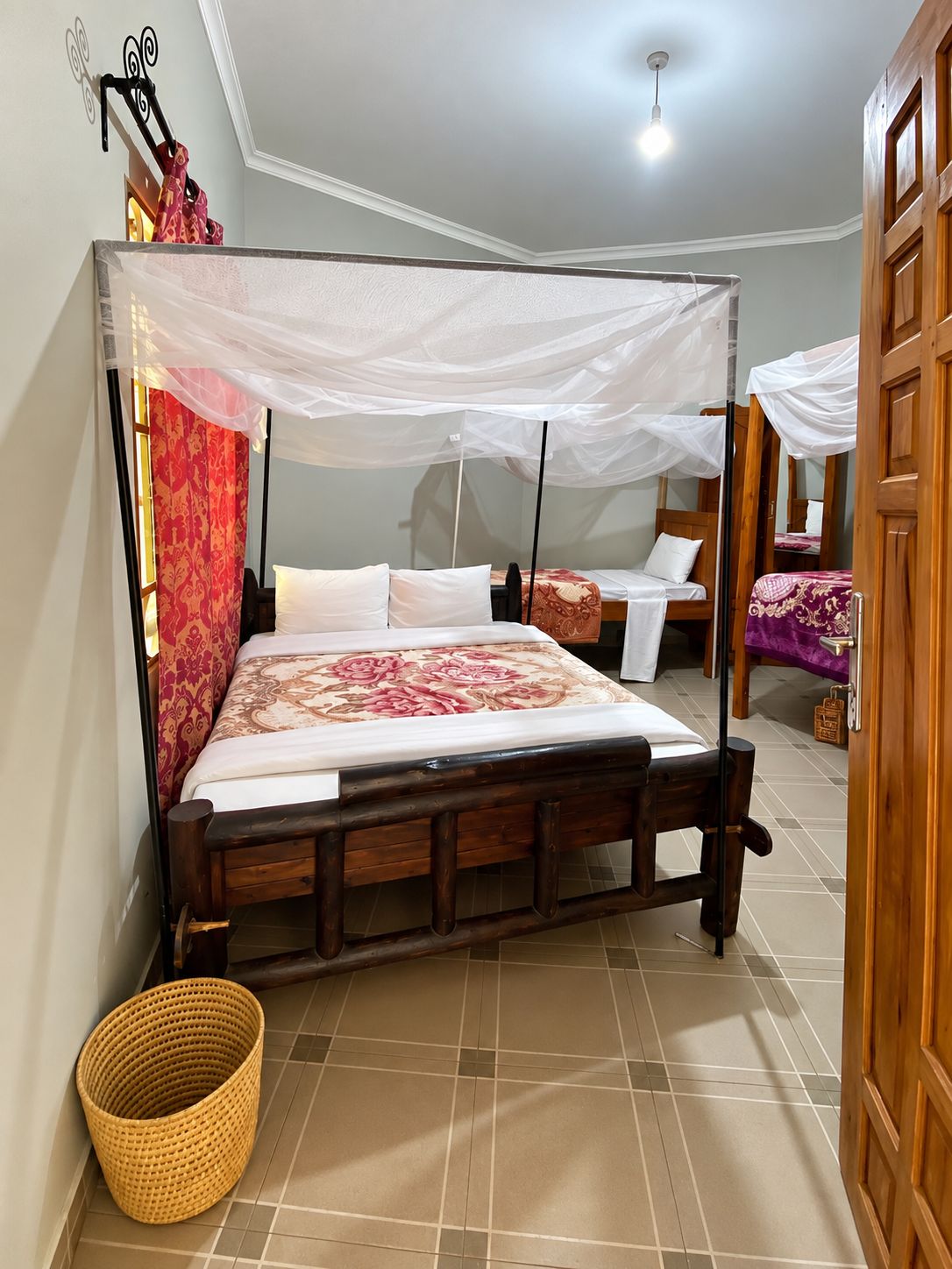 A room with a bed under a mosquito net, a wooden door, and a tiled floor.