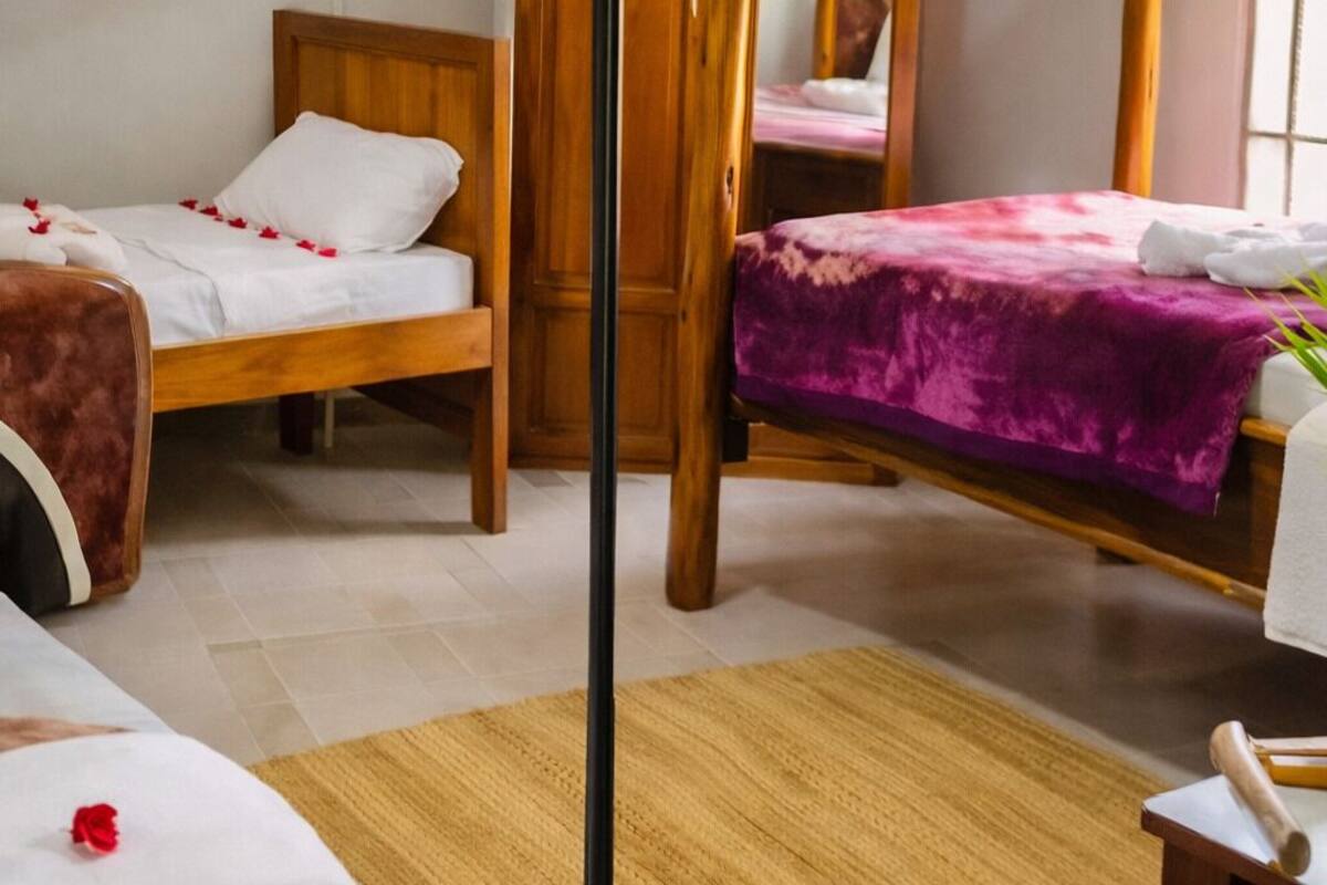 Una habitación con dos camas, una con cabecera de madera y la otra con dosel.