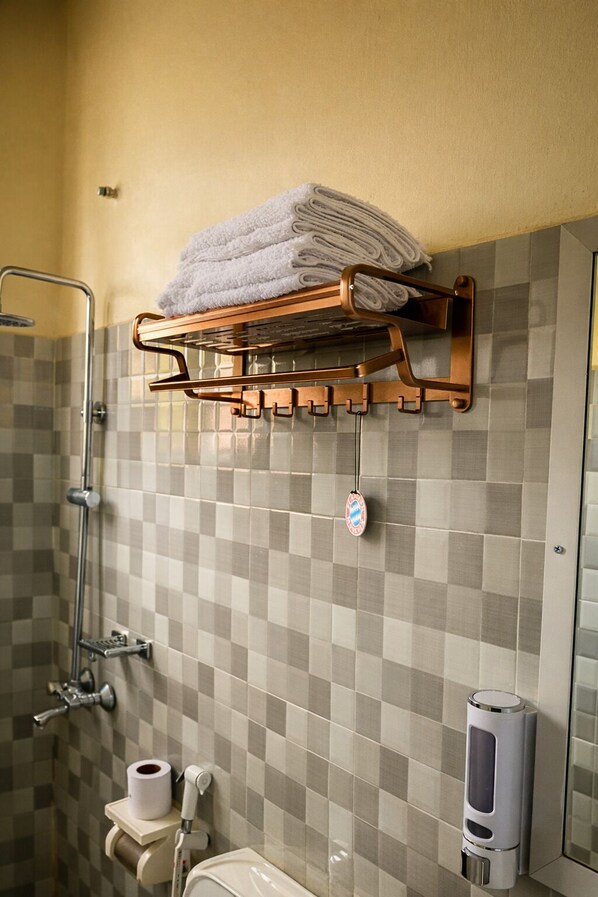 Un baño con pared de baldosas a cuadros, un perchero con toallas dobladas, un dispensador de papel higiénico y un dispensador de jabón.