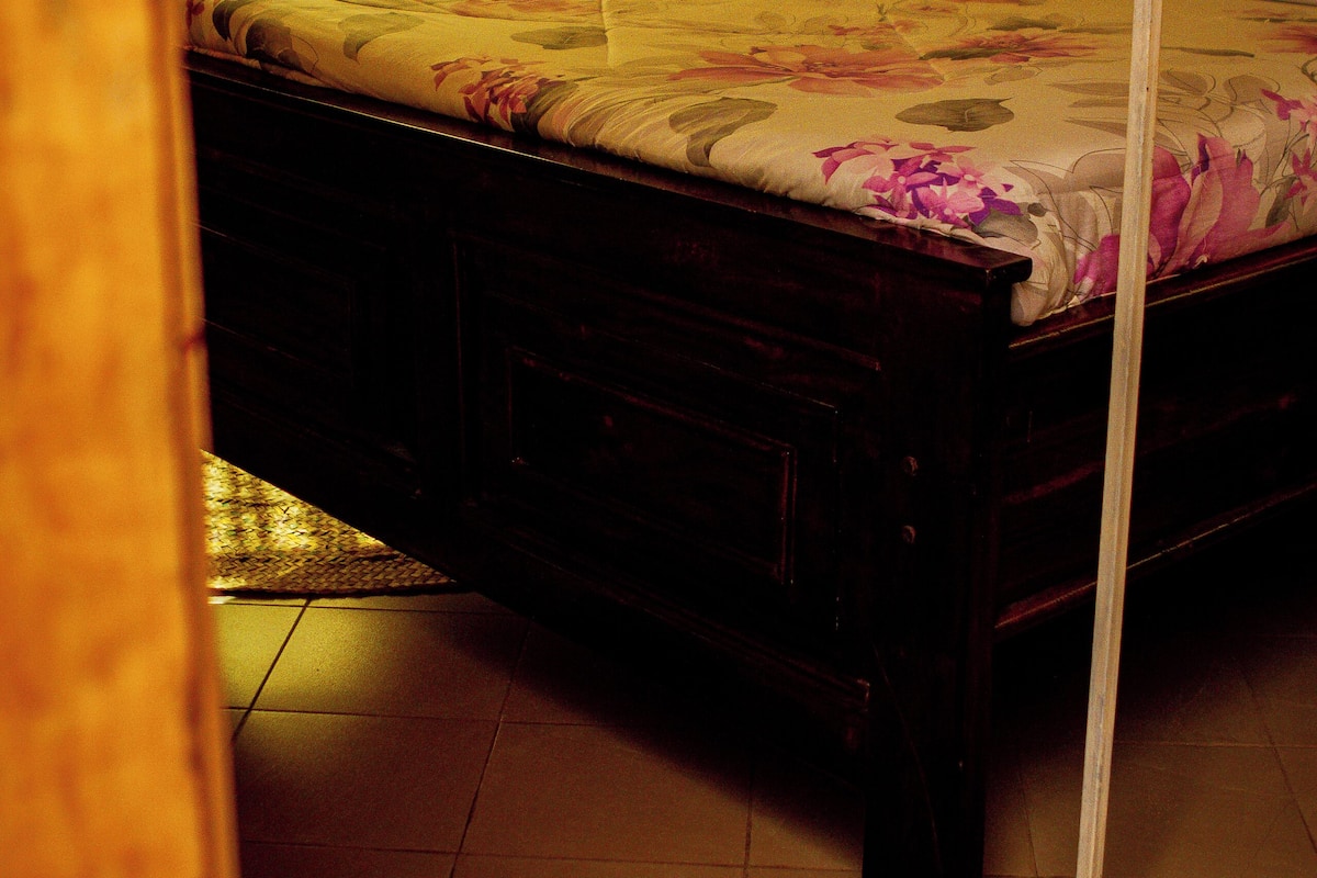 Una cama con dosel, cabecera de madera y colcha estampada con flores.