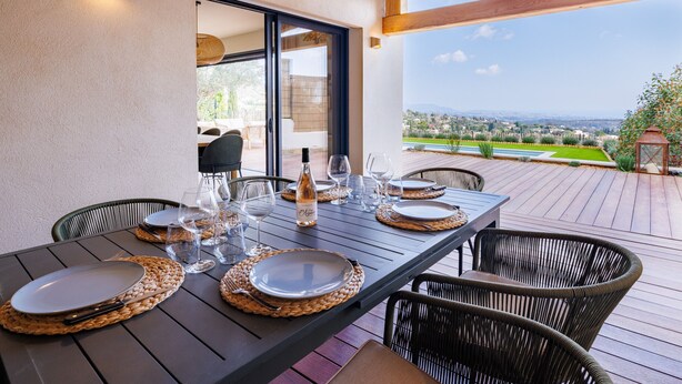 Un espace de restauration en plein air avec une table dressée pour quatre personnes, entourée de chaises en osier, et offrant une vue sur un paysage pittoresque.