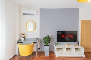 A modern living room with a grey wall, a white entertainment unit, a yellow chair, a desk, a potted plant, and a flat-screen TV displaying "NETFLIX". - Riccardo's cottage 6 minutes from the lake + Parking (Nesso)