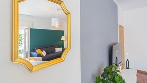 A room with a large golden-framed mirror, a dark green sofa, a white lamp, and a potted plant.