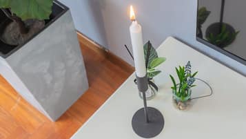 A white candle on a black holder on a white table, with a potted plant and a small glass container with a plant on the table.