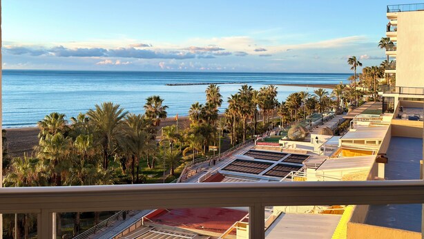 Ett hotell vid stranden med utsikt över havet, palmer och stranden.