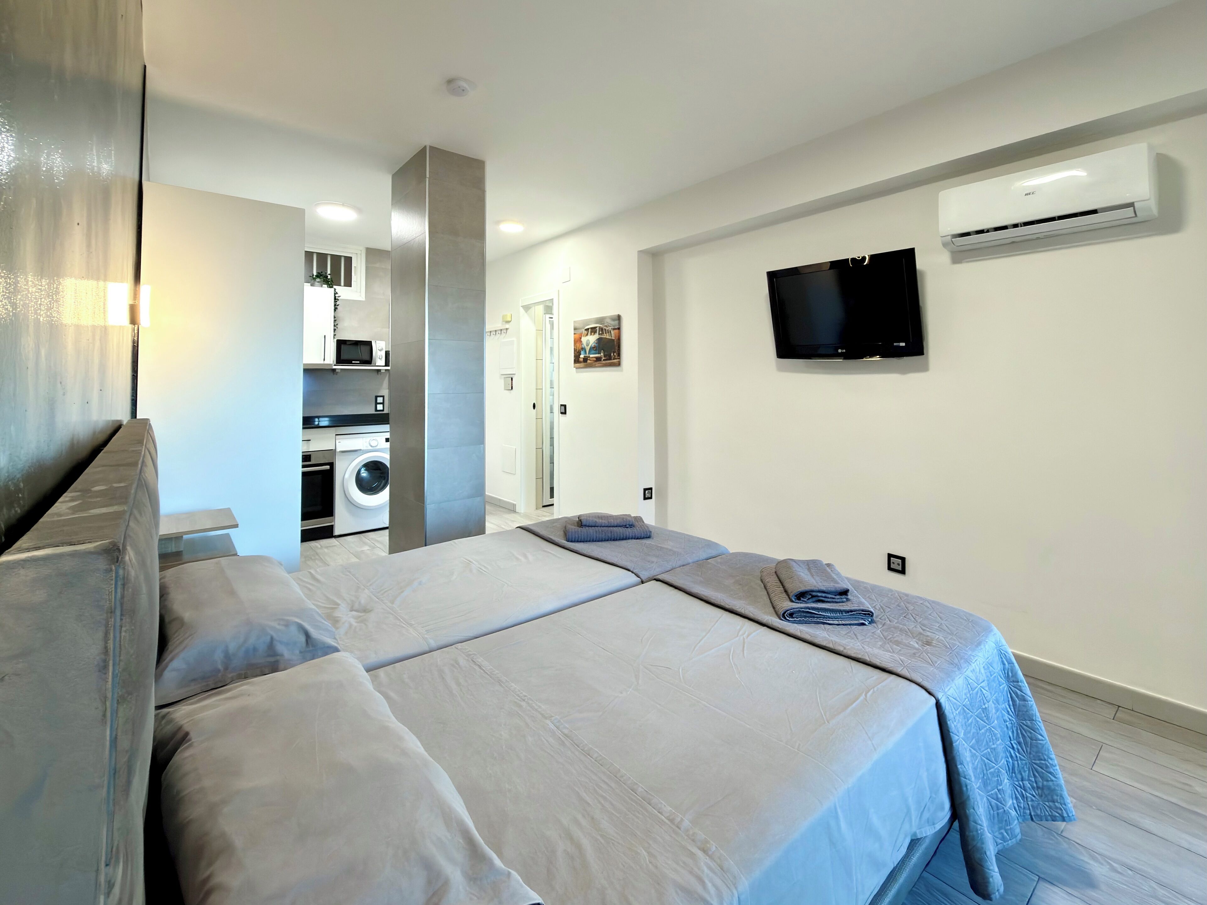 Une chambre d’hôtel moderne avec un grand lit, un téléviseur fixé au mur et un appareil de climatisation.