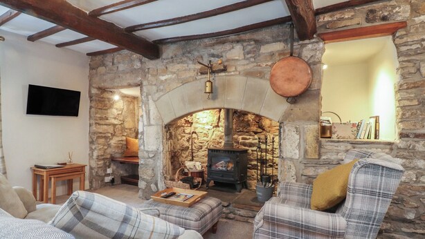 A cozy living room with a stone fireplace, plaid furniture, and a flat-screen TV mounted on the wall. - Chamber End Fold (Skipton)