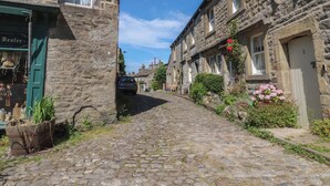 Una calle adoquinada en un pueblo histórico, con edificios de piedra, un coche aparcado y una tienda con puerta verde.