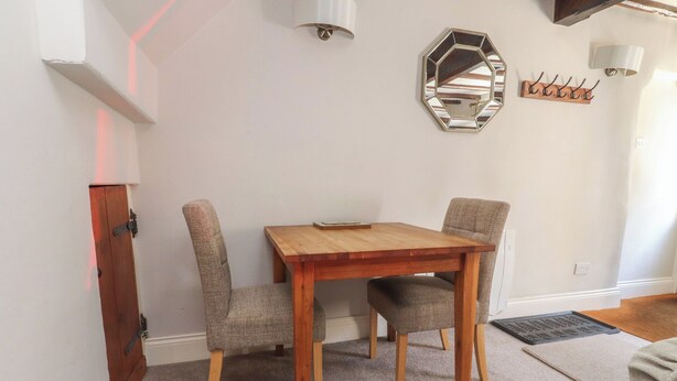 Un comedor con una mesa de madera y dos sillas, un espejo en la pared y un perchero.