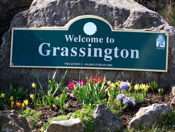 Un cartel de bienvenida a Grassington, con un letrero de límite de velocidad y flores en primer plano.