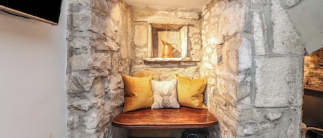 Una nicchia in pietra con una panchina, cuscini, un caminetto e un televisore.