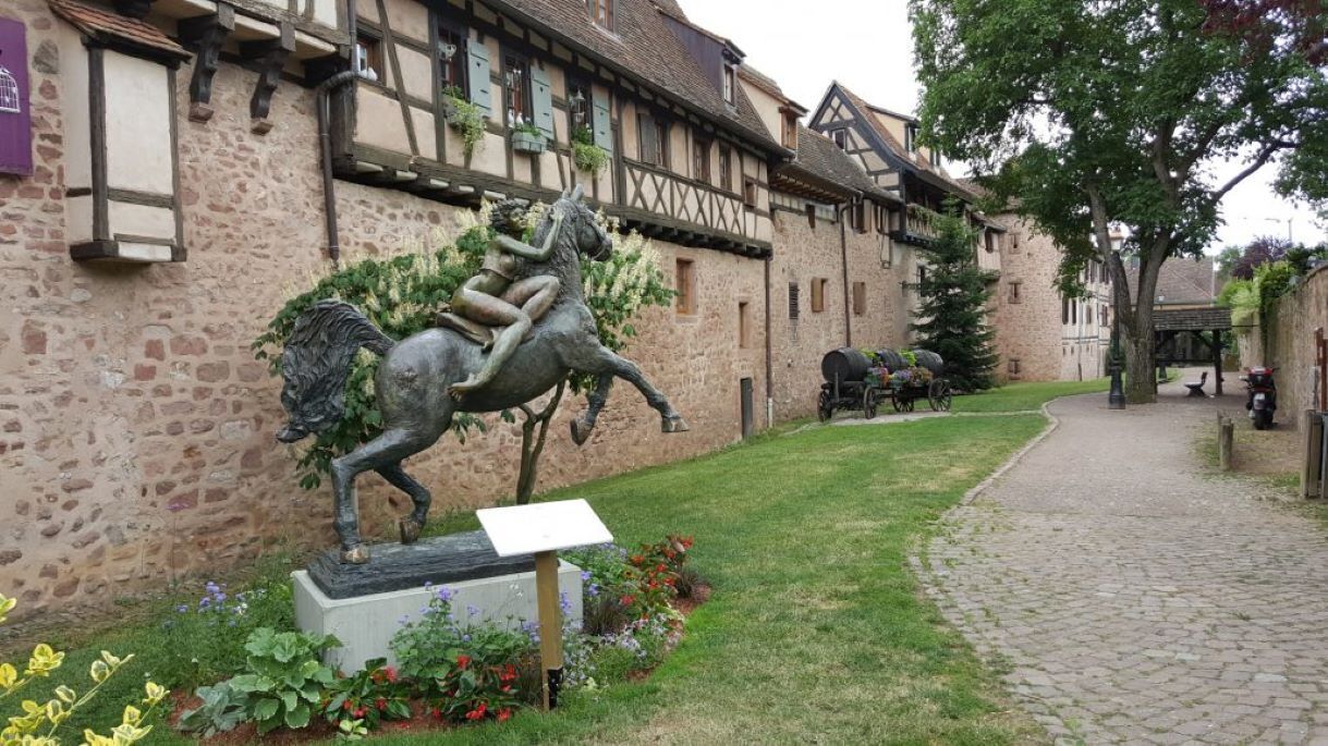 Ein Kopfsteinpflasterweg führt zu einem Gebäude mit einer Pferdestatue und einem Schild.