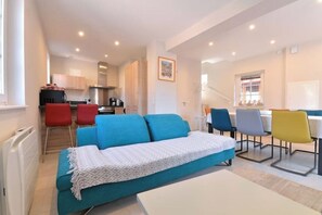 Una sala de estar moderna con un sofá, una mesa de comedor y sillas. Se observa un área de cocina al fondo.