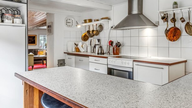 Eine moderne Küche mit weißen Schränken, einer Granitarbeitsplatte, einer Edelstahl-Dunstabzugshaube und hängenden Töpfen.