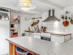 Une cuisine moderne avec des armoires blanches, un comptoir en granit, une hotte de cuisinière en acier inoxydable et des casseroles suspendues.