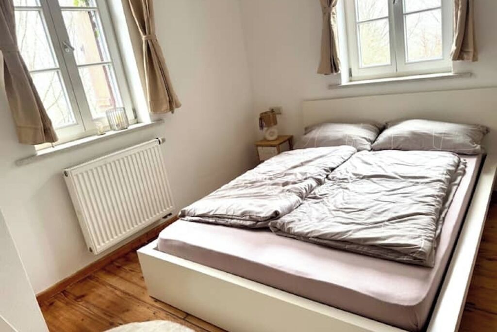 Un dormitorio con cama, mesita de noche, ventana con cortinas y radiador.