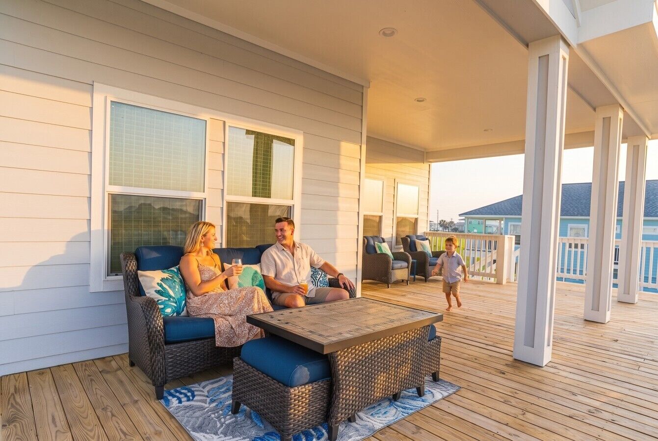 Um terraço coberto ao ar livre com móveis de vime, uma mesa de madeira e vista para o mar.