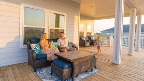 A covered outdoor deck with wicker furniture, a wooden table, and a view of the ocean. - Indian Sunrise- peaceful/short stroll to beach! (Galveston)