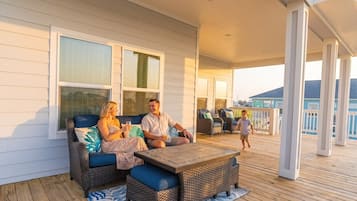 Um terraço coberto ao ar livre com móveis de vime, uma mesa de madeira e vista para o mar.