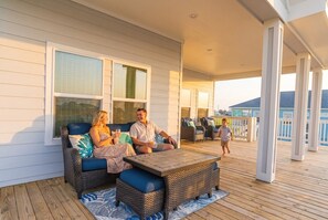 A covered outdoor deck with wicker furniture, a wooden table, and a view of the ocean. - Indian Sunrise- peaceful/short stroll to beach! (Galveston)