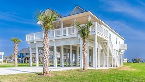 A two-story beachfront house with a balcony, palm trees, and a clear blue sky. - Indian Sunrise- peaceful/short stroll to beach! (Galveston)